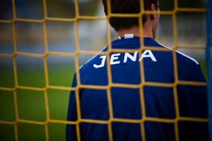 Fußballer durch Tornetz fotografiert, auf T-Shirt steht Jena