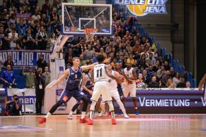 Männer spielen Basketball vor Publikum. 