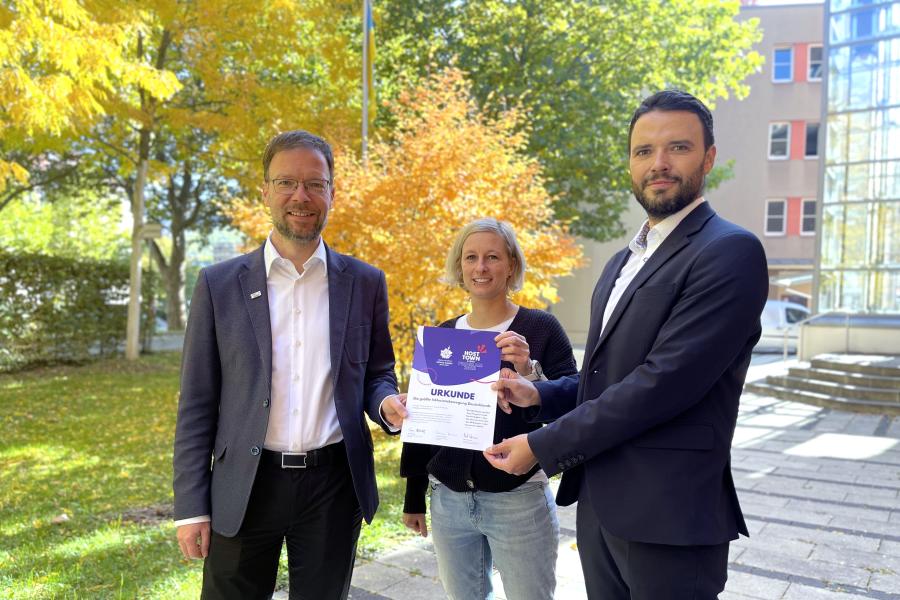 Drei Personen mit Ernennungsurkunde für das Host Town Program